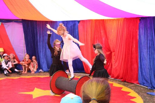 Im Zirkuszelt: Mädchen auf eine Balancerolle, zwei andere Mädchen unterstützen