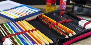 geöffnete Schulmappe mit bunten Stiften, Lineal und Radiergummi, im Hintergrund Anspitzer und Klebstift
