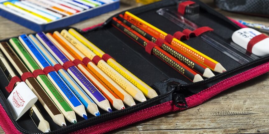 geöffnete Schulmappe mit bunten Stiften, Lineal und Radiergummi, im Hintergrund Anspitzer und Klebstift
