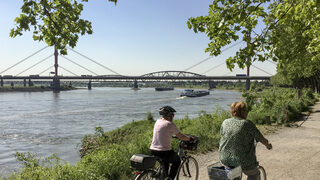 Älterer Mann und ältere Frau fahren mit dem Fahrrad am Rhein entlang