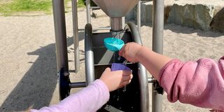 Kinder halten Formen unter eine Wasserrinne auf einem Wasserspielplatz