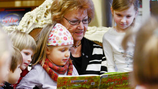 Frau liest Kindern aus einem Buch vor.
