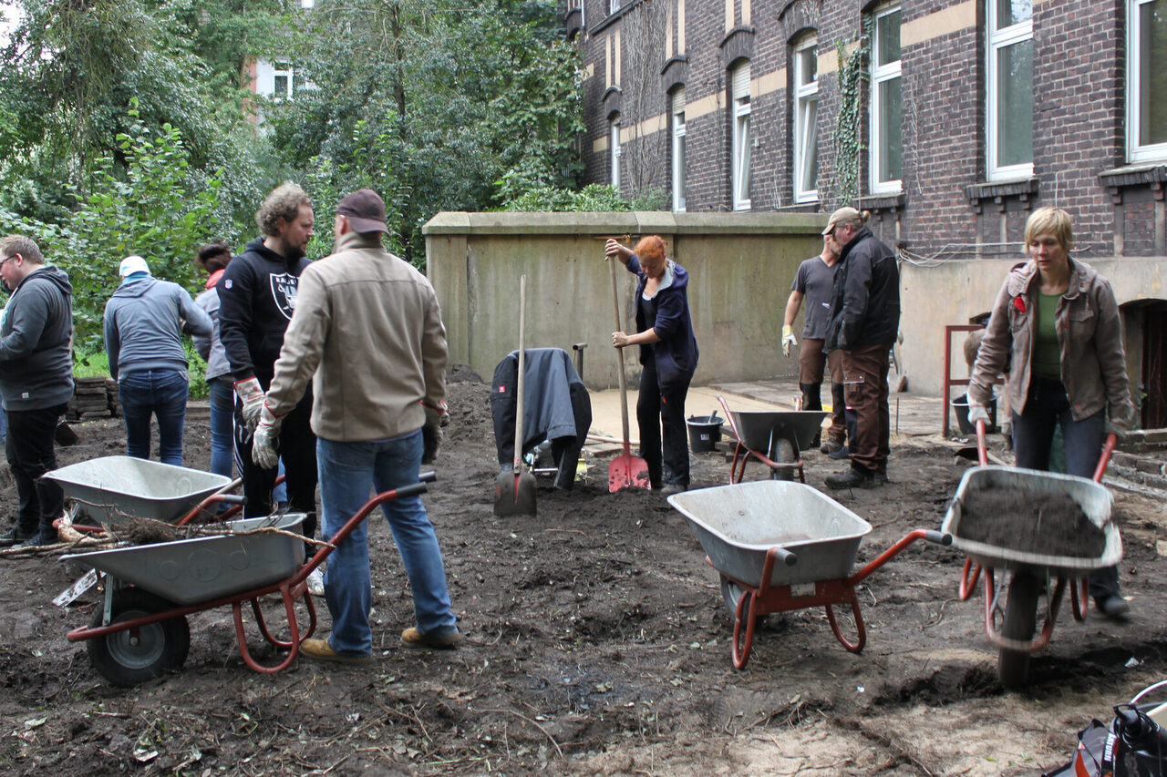 Männer und Frauen befüllen Schubkarren mit Erde.