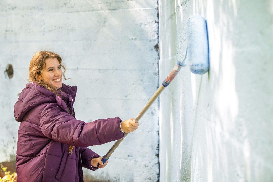 Eine Mitarbeiterin streicht eine Wand mit weißer Farbe