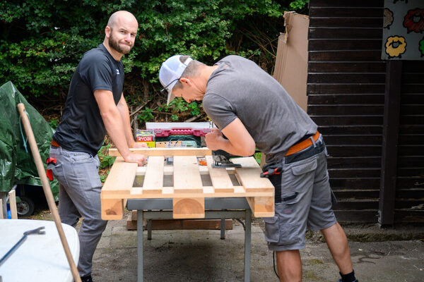 Zwei Männer schneiden Holzpaletten zu.