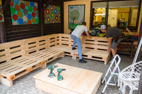Zwei Männer bauen aus Holzpaletten eine Sitzecke.