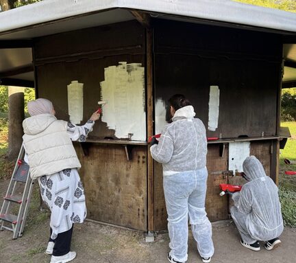 Mitarbeitende der Targo Bank streichen eine Hütte mit weißer Farbe an.