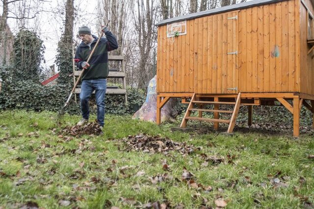 Ein Mitarbeiter der TARGOBANK fegt mit einem Rechen das Laub im Außengelände zusammen.