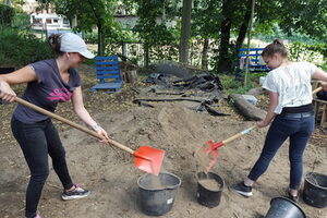 zwei Frauen schaufeln Erde in einen Eimer