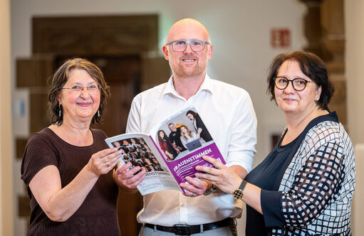 Drei Menschen halten eine Broschüre fest
