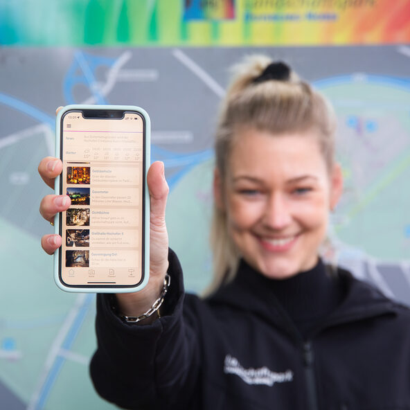Junge Frau zeigt auf dem Smartphone den digitalen Guide durch den Landschaftspark