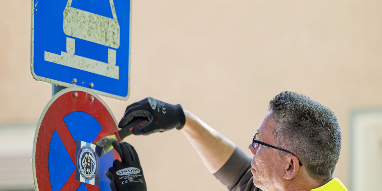 Mitarbeiter entfernt Aufkleber von einem Straßenschild