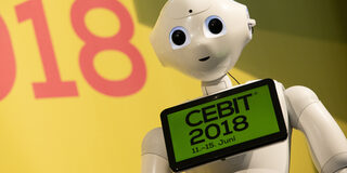 Roboter mit umgehängten Tablet. Aufschrift: CEBIT 2018. 11-15. Juni