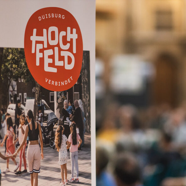 Hochfeld Logo im Vordergrund mit Gruppe von Menschen dahinter