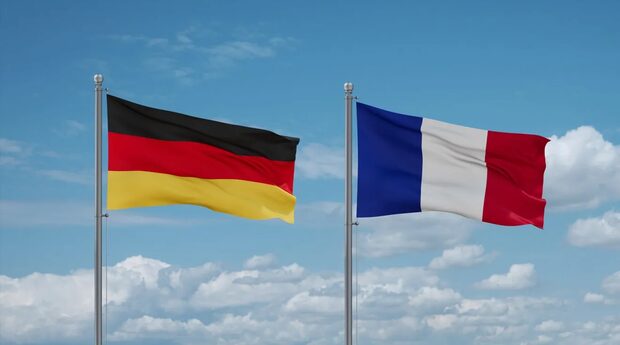 links eine Deutschlandflagge vor blauem Himmel gehisst, rechts daneben eine Frankreichflagge