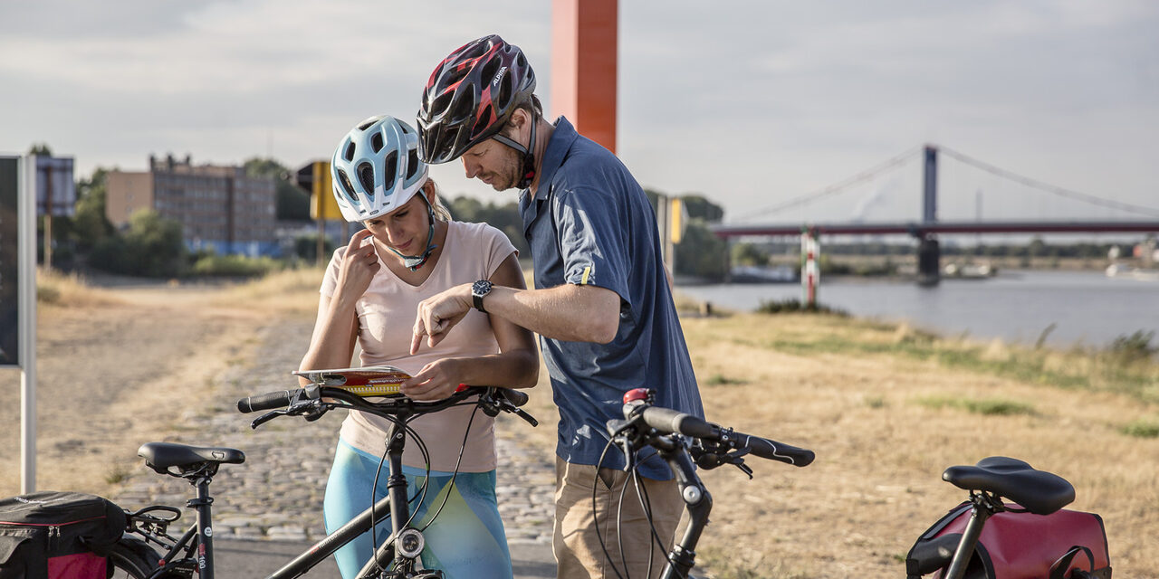 Eine Radfahrerin und ein Radfahrer stehen neben ihren Fahrrädern vor der Rheinorange in Duisburg.