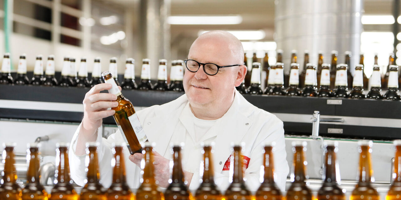 Ein Mann im Kittel steht in der König-Brauerei an einem Fließband mit Bierflaschen.