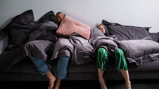Ein Mann und eine Frau unter Decken und Kissen auf einem Sofa