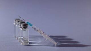 Eine Spritze lehnt an Flaschen mit Impfdosen