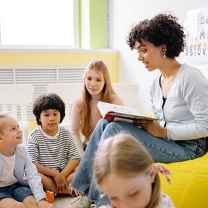 Eine Frau liest mehreren Kindern aus einem Buch vor